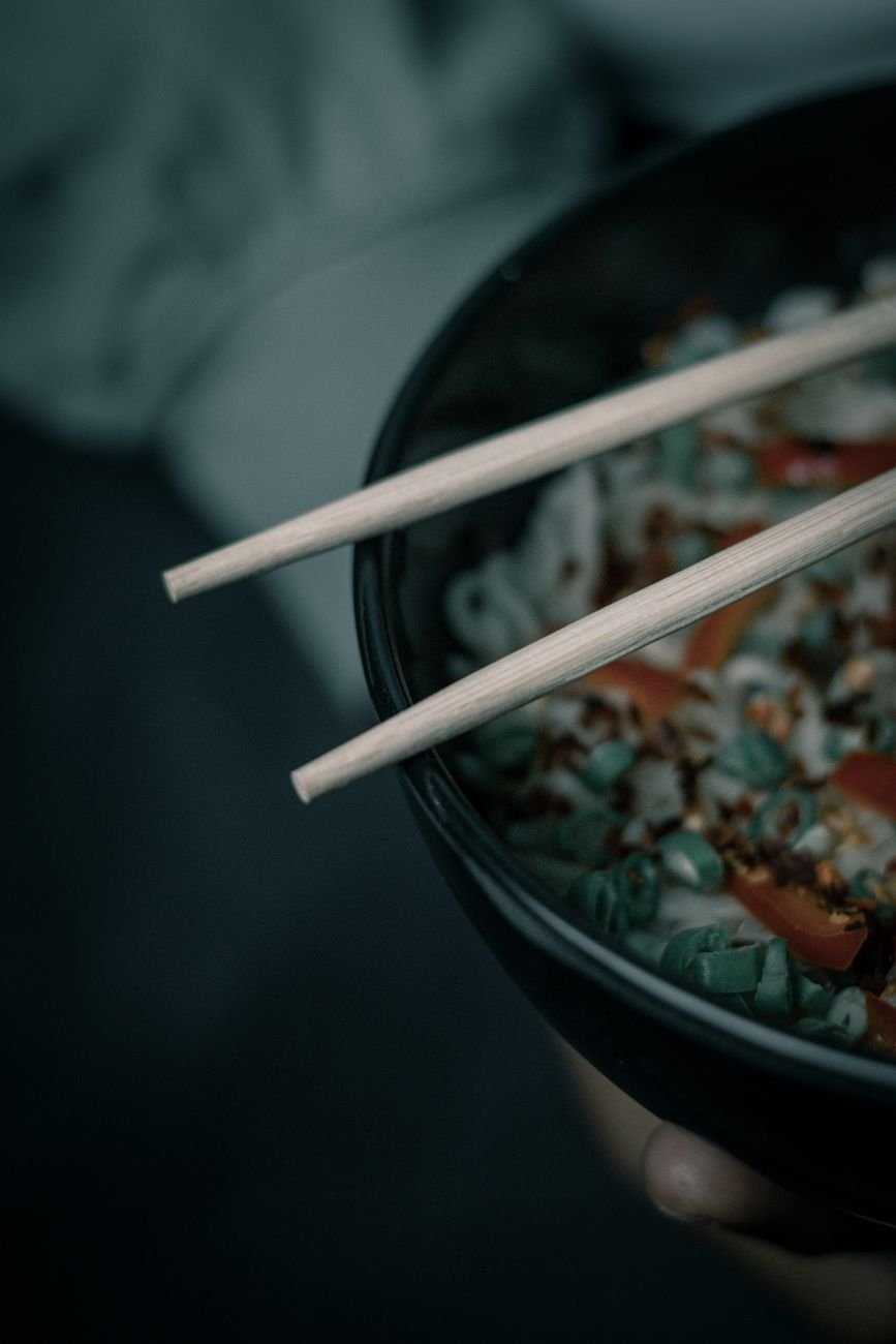Dark moody close-up of a noodle bowl with chopsticks, perfect for Asian cuisine themes