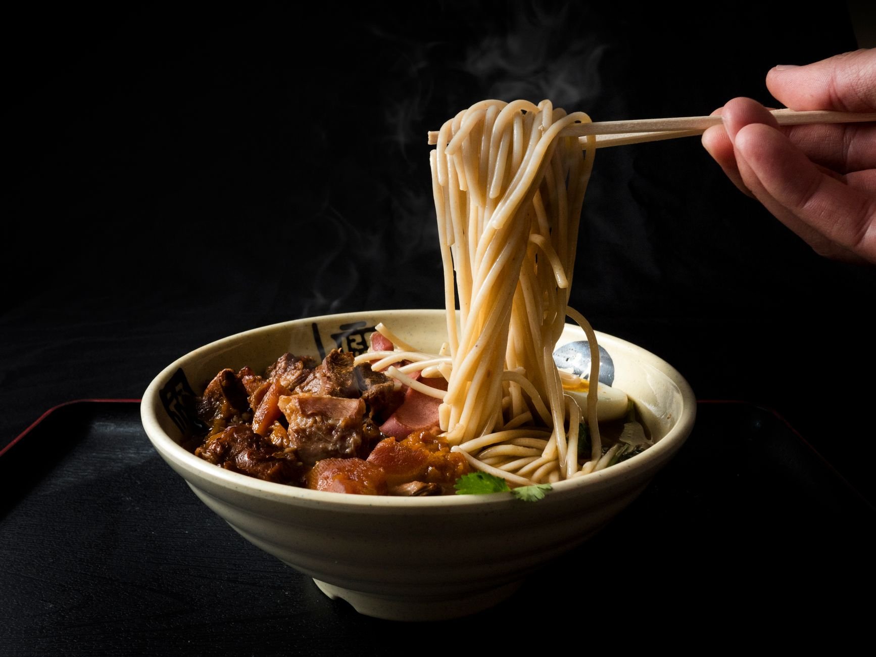 A steaming bowl of KOJA ramen with beef lifted by chopsticks